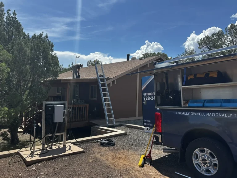 Nickel Roofing service truck parked in driveway with technician working on rooftop in the background